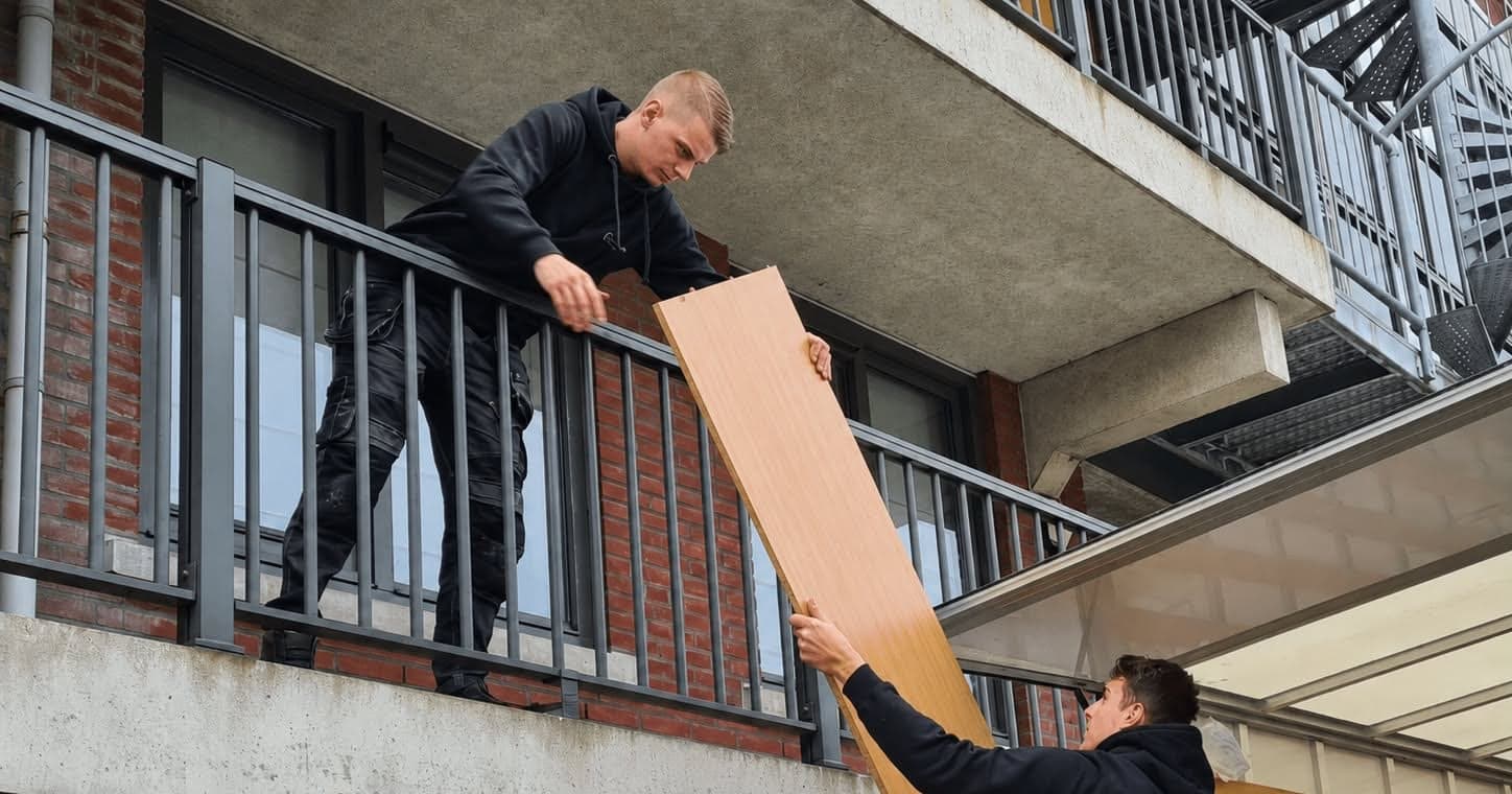 Twee verhuizers tillen een meubelpaneel omhoog naar het balkon van een appartement